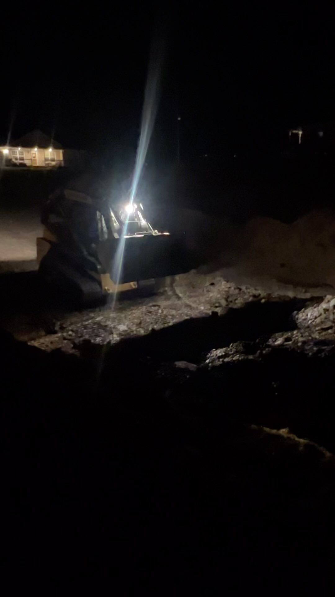 A tractor plowing snow at night, illuminated by its bright headlights.