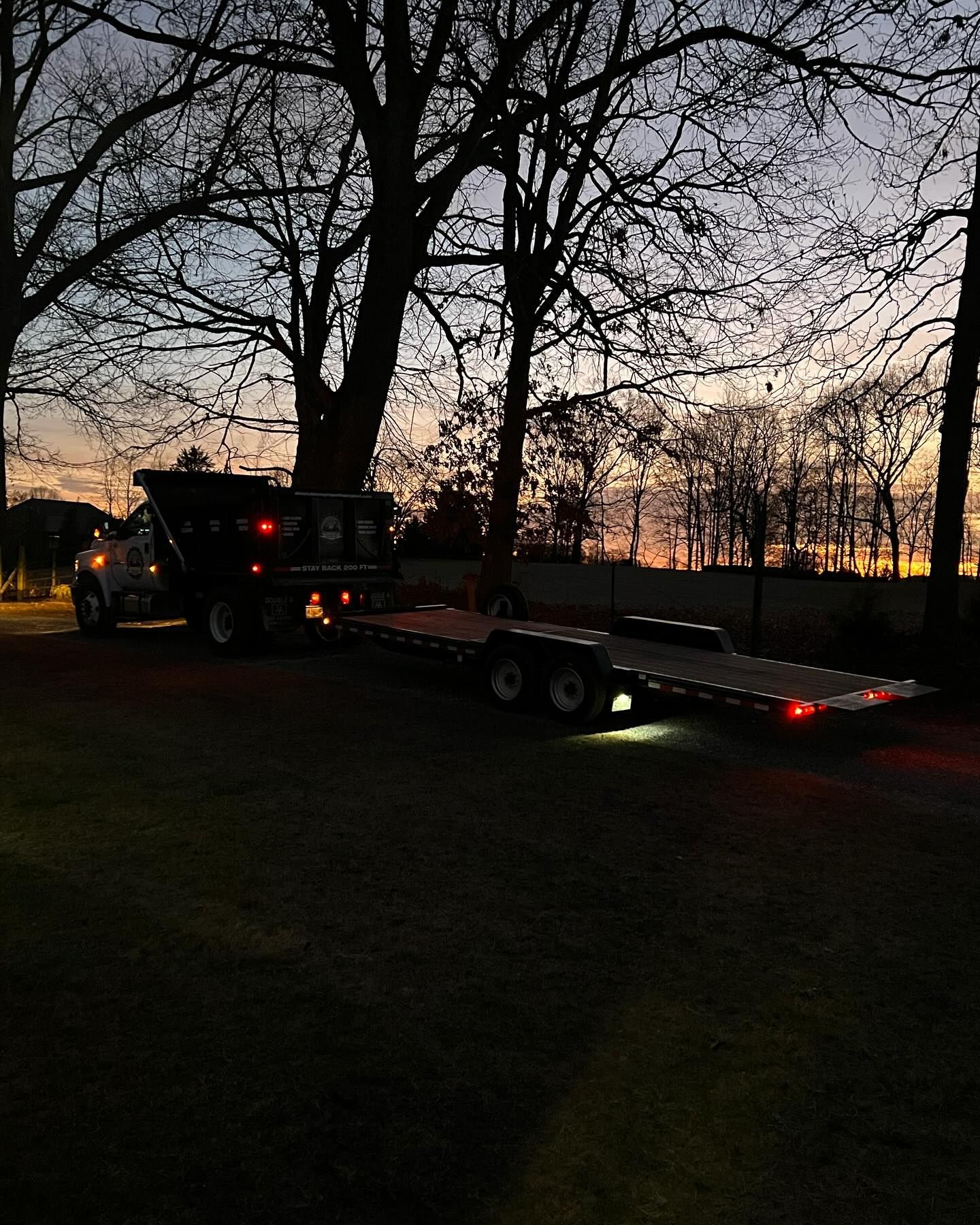 A truck pulling a dump trailer and a flatbed trailer at dusk.