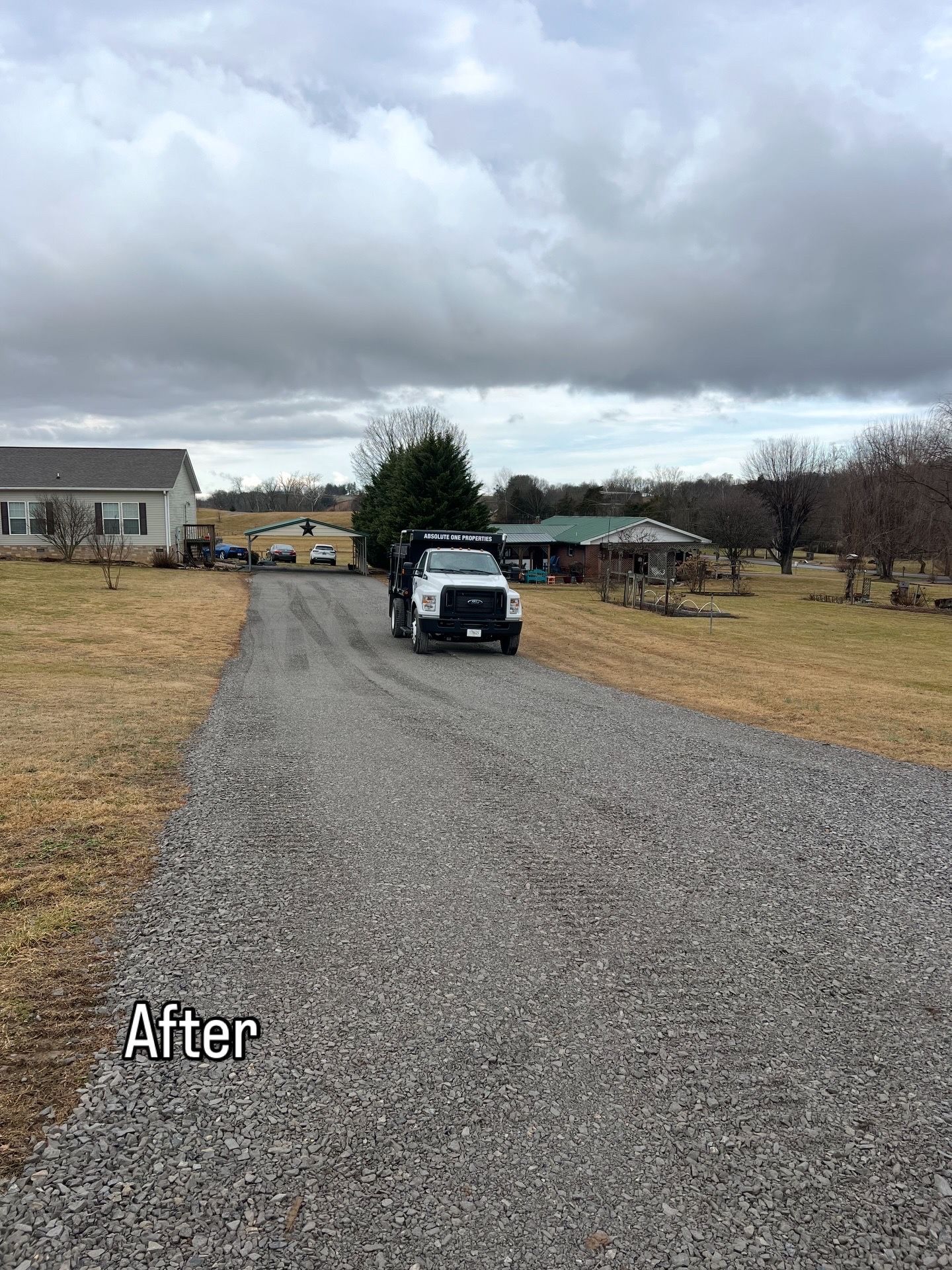 A gravel driveway with a dump truck and houses in the background on a cloudy day.