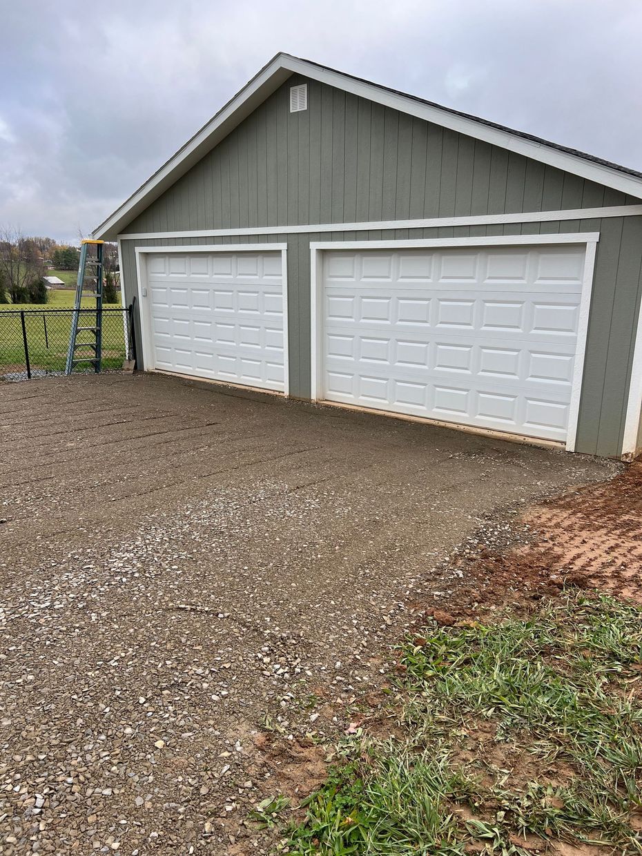 Two-car garage with white doors, green siding, gravel driveway, and overcast sky.