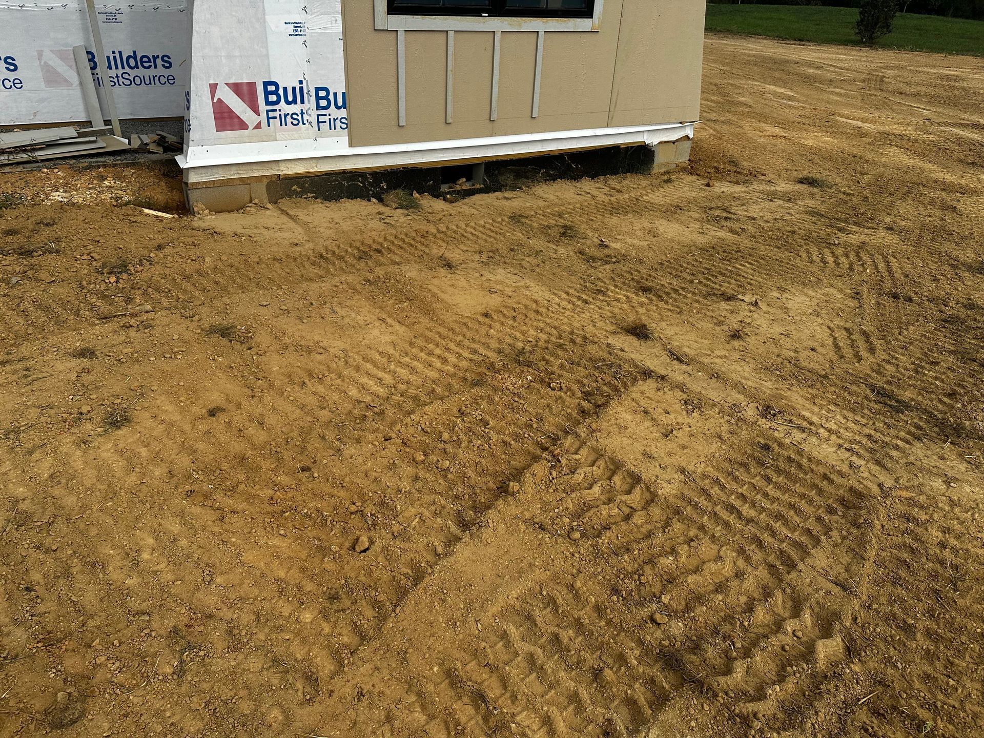Construction site. A small building with light brown siding, on a dirt and wood chip surface.