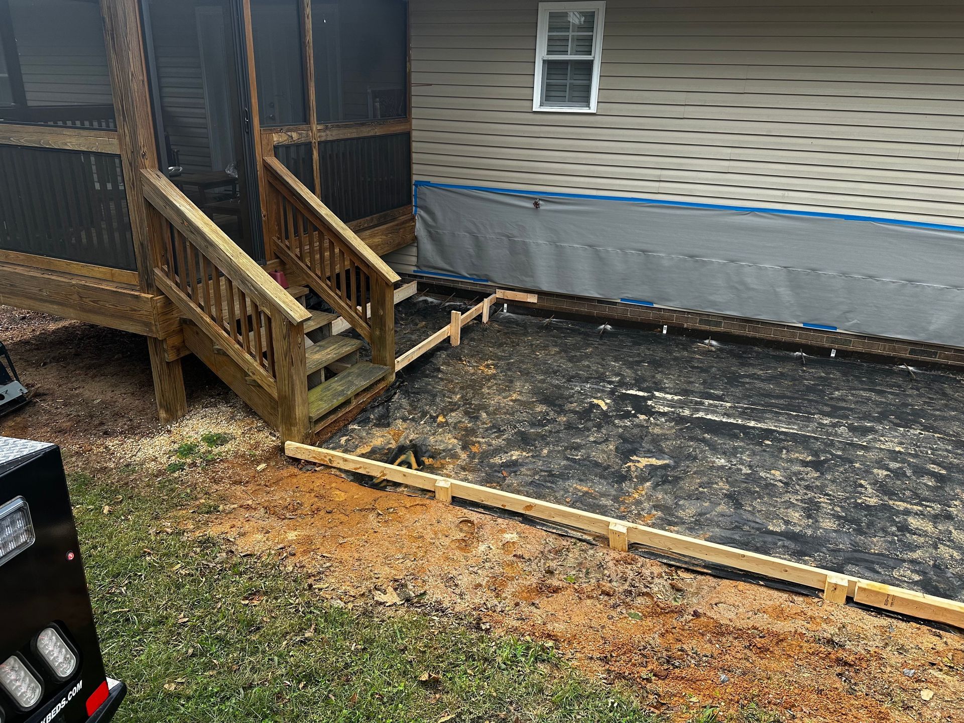 Wooden deck with stairs next to a house with new concrete framework in yard.