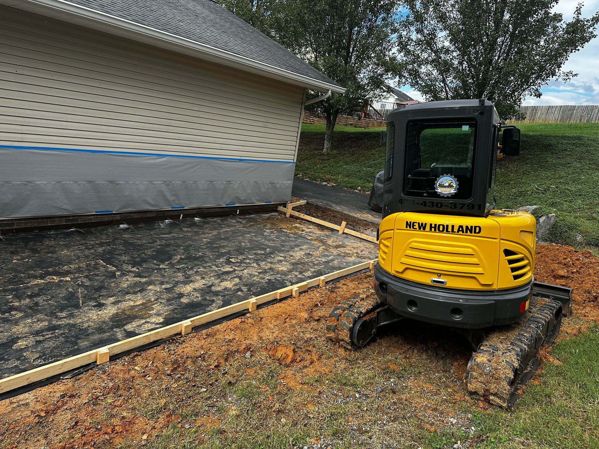 Yellow excavator next to a framed-out concrete pad near a house, preparing for construction.