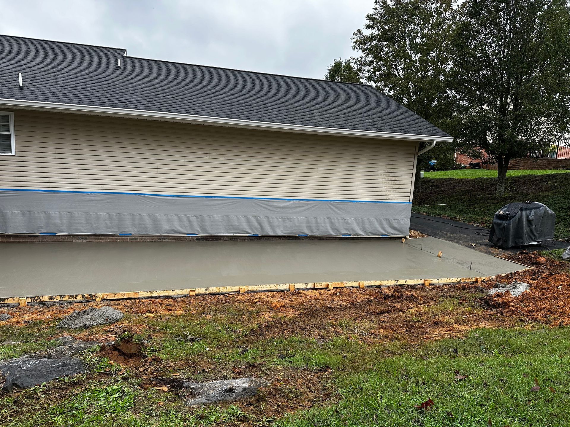 Newly poured concrete patio next to a house with exposed sheathing; overcast sky.