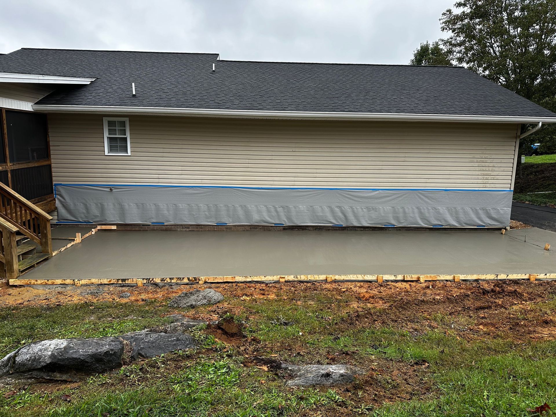 Exterior view of a house with a newly poured concrete patio; tan siding, gray roof, and overcast sky.