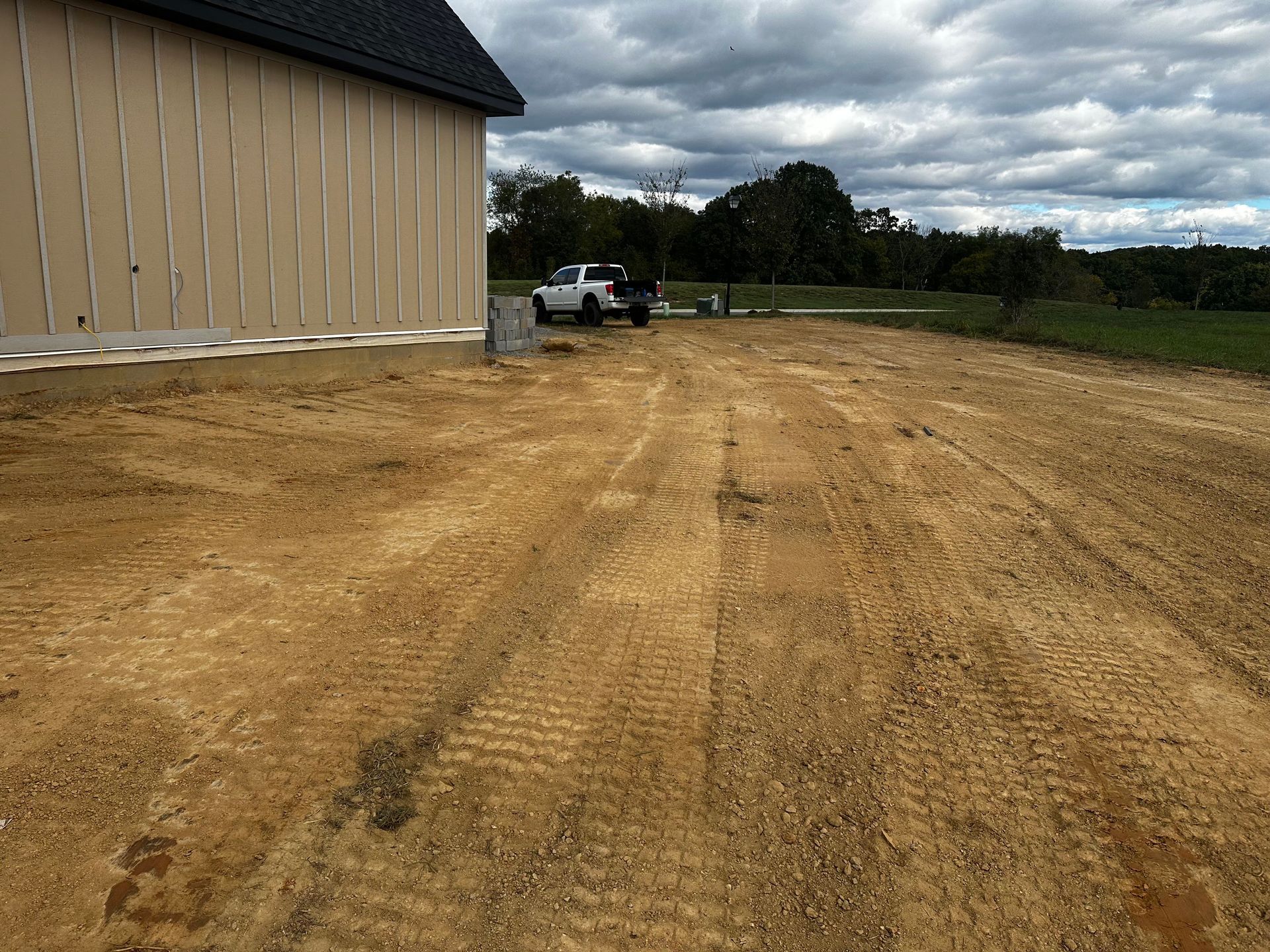 A gravel driveway beside a light-colored building under a cloudy sky. A white pickup truck is parked nearby.