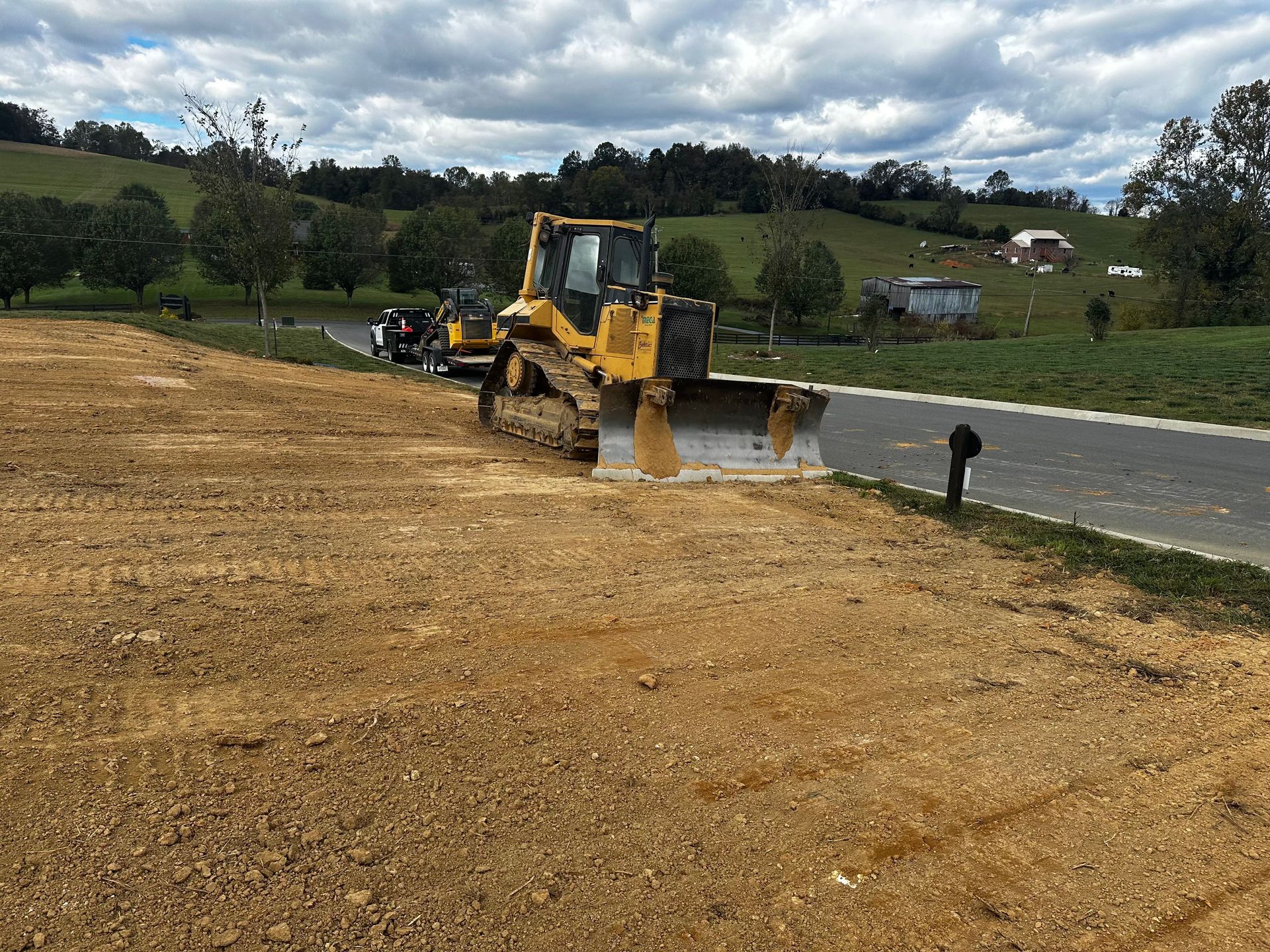 Yellow bulldozer grading dirt next to a road, under a cloudy sky.