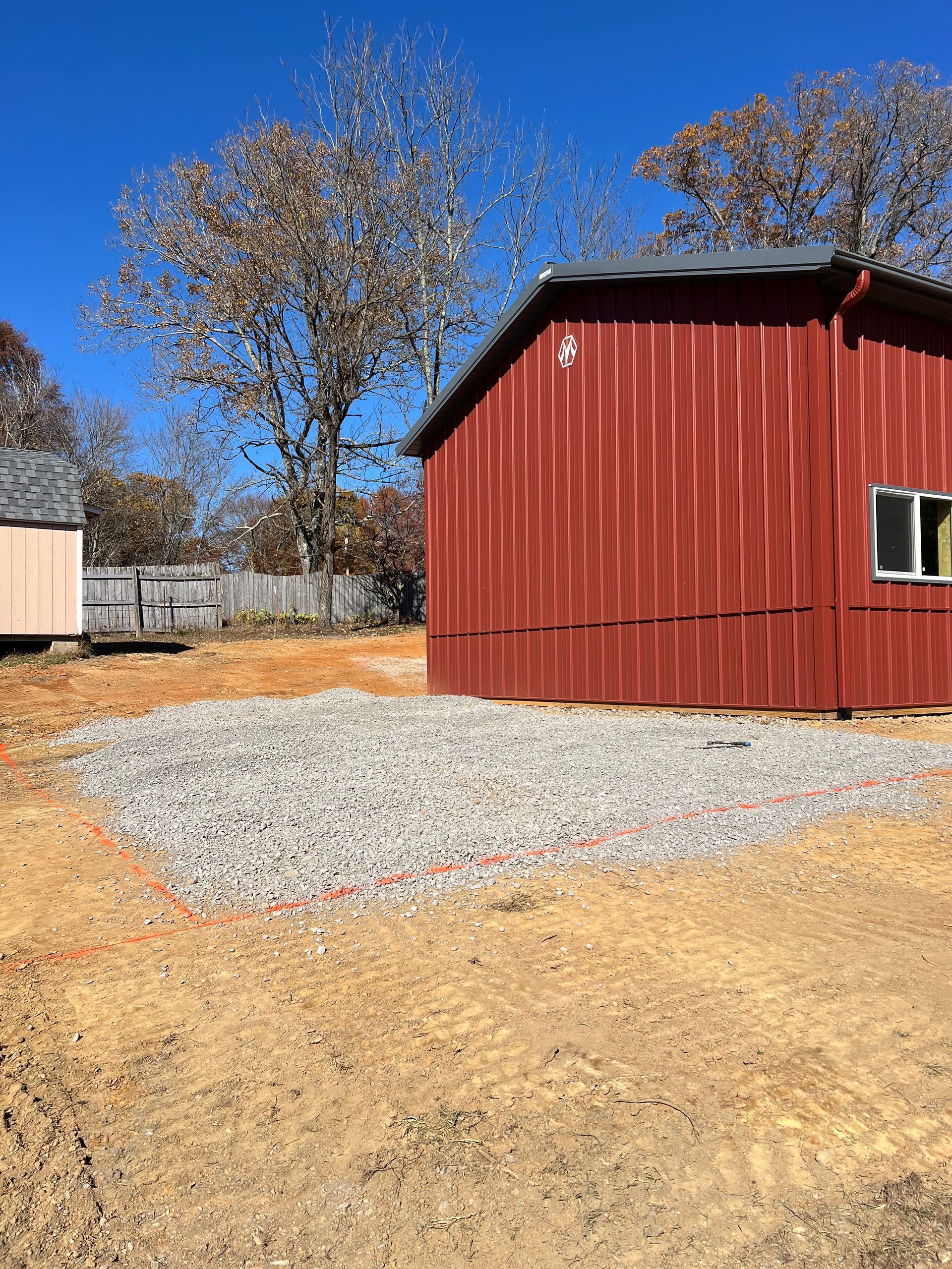 Gravel-filled area outlined in red, next to a red building under a clear blue sky.