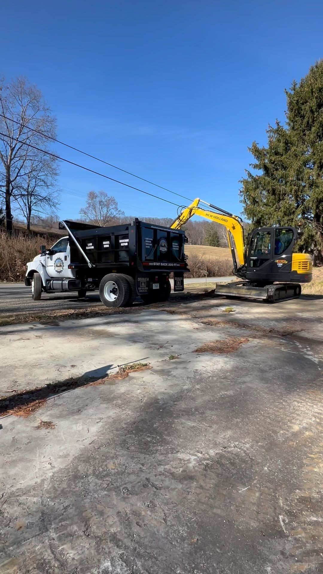 Excavator loading a dump truck on a paved road under a blue sky.