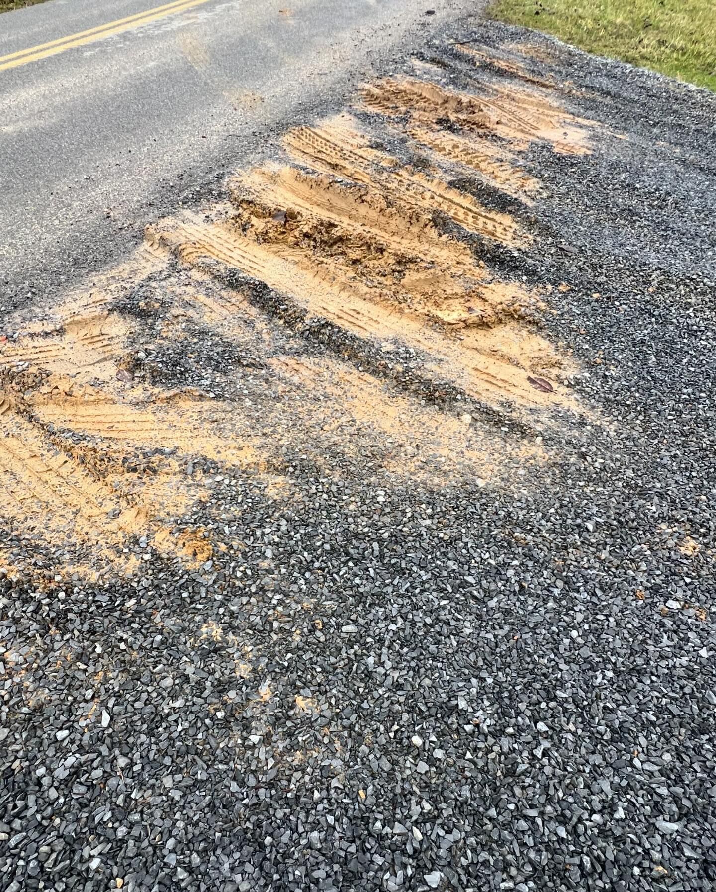 Gravel roadside with tire tracks in exposed dirt alongside a paved road.