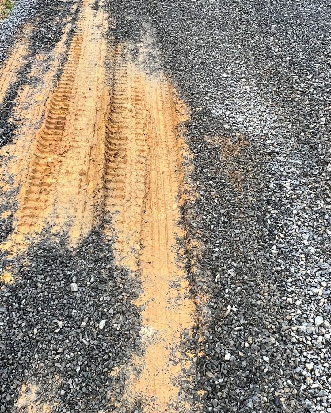 Tire tracks in orange dirt on a gravel road.