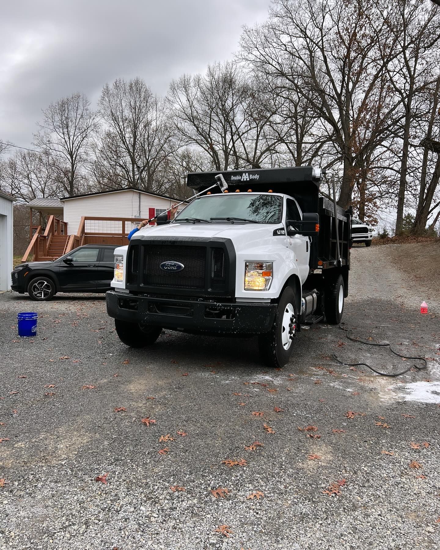 White dump truck parked on a gravel driveway. Black pickup truck is visible to the left.