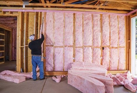 Man installing pink insulation between wooden wall studs in a new construction setting.