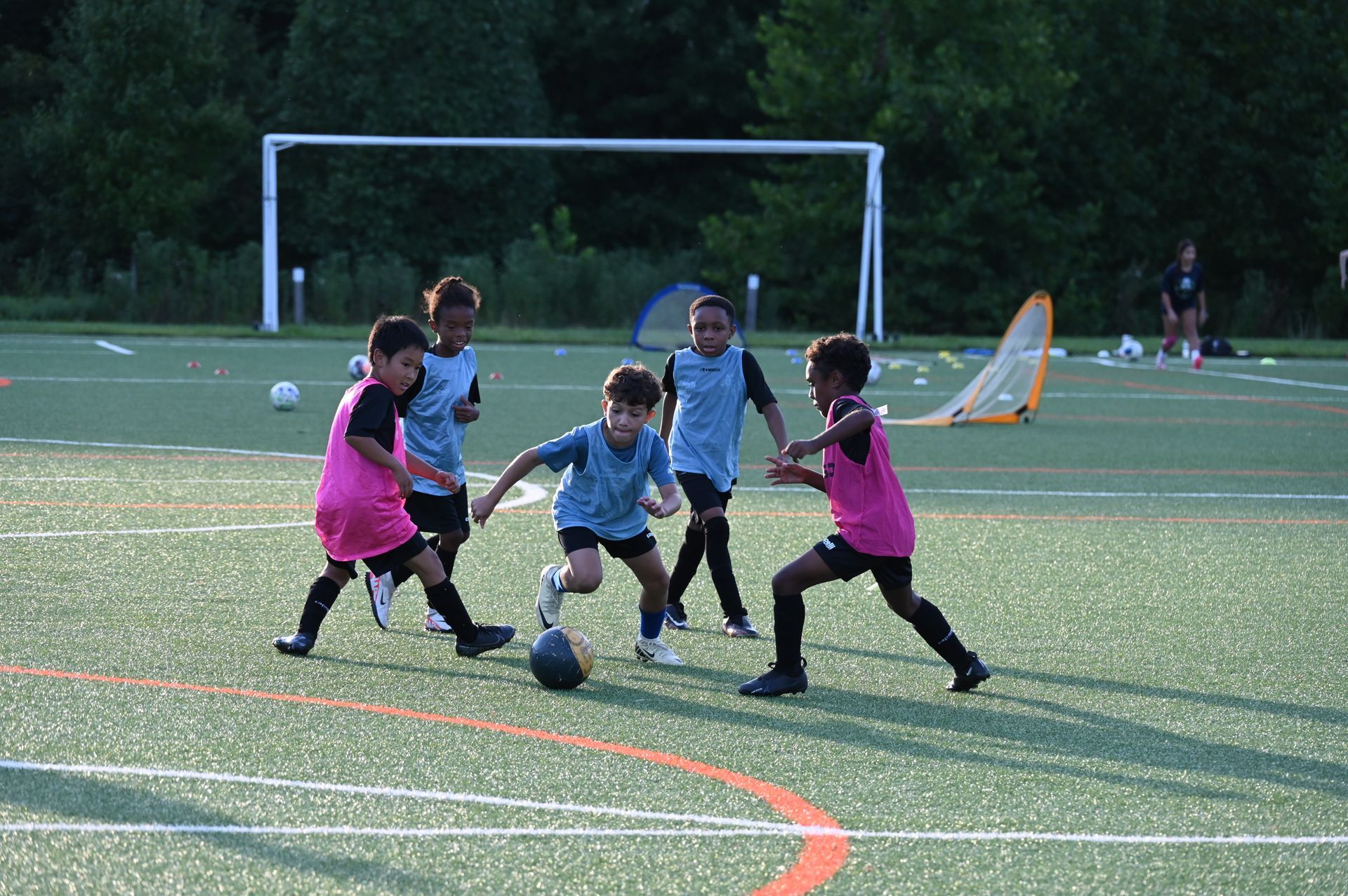 MSI soccer youth players in blue and pink pinnies compete for the ball on turf field during practice drills under the sun.