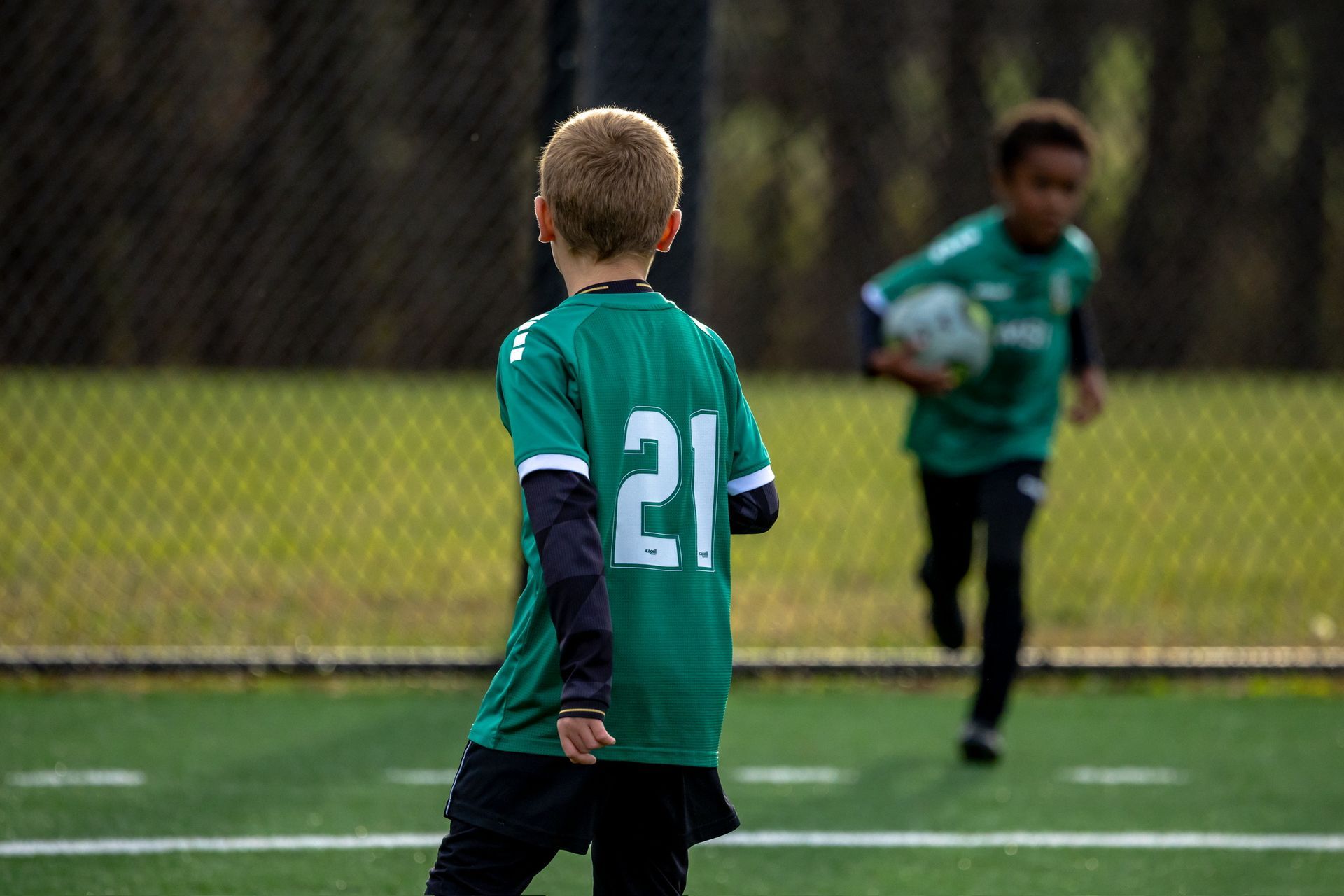 Two young MSI soccer players in green uniforms on the field, one holding the ball