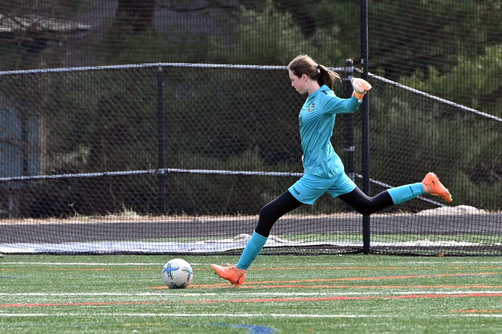 MSI soccer goalkeeper in teal uniform kicks the ball downfield during a match, showing strong form and focus on turf field.
