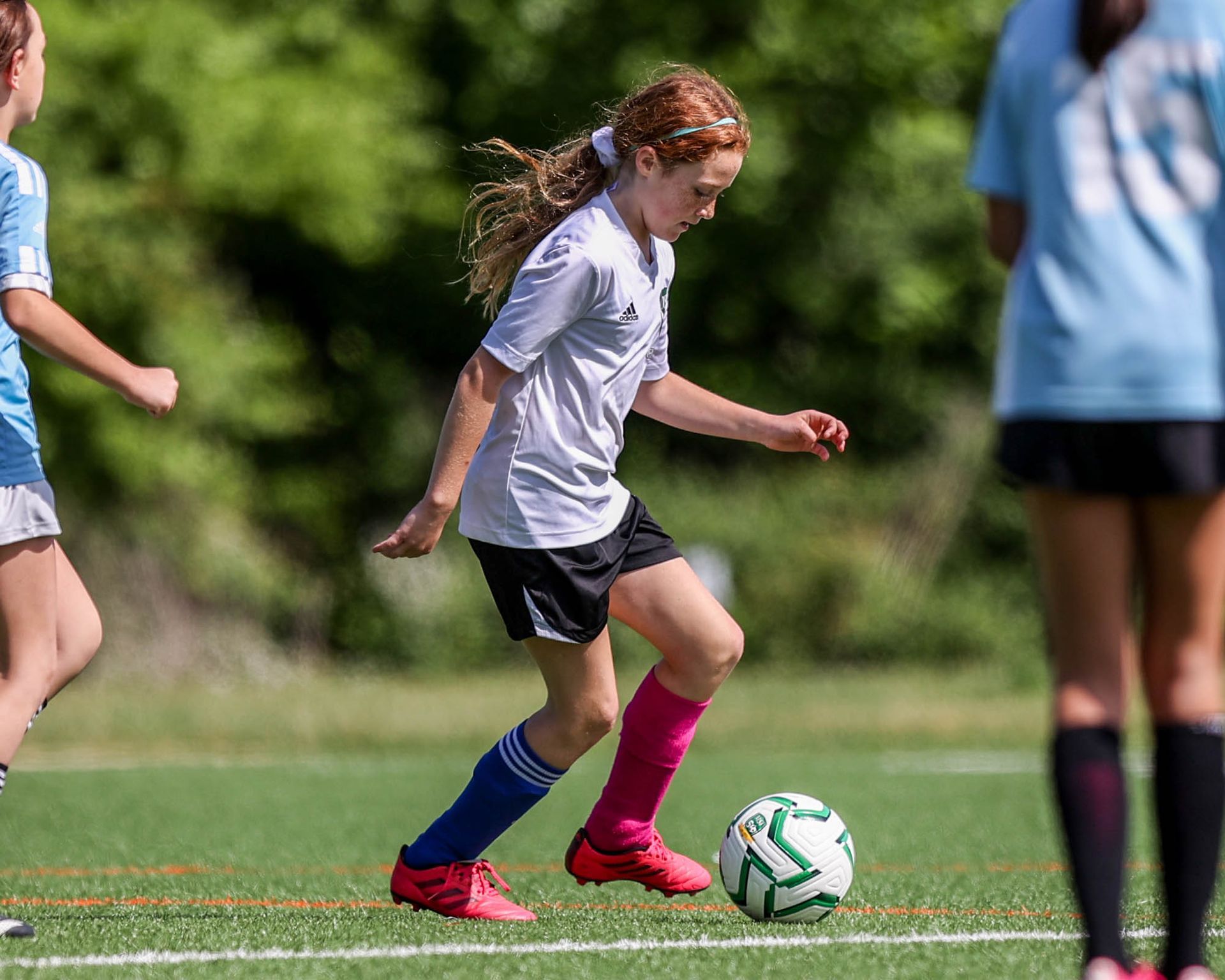MSI youth soccer player in white jersey and pink socks kicks the ball on turf field during a competitive match.