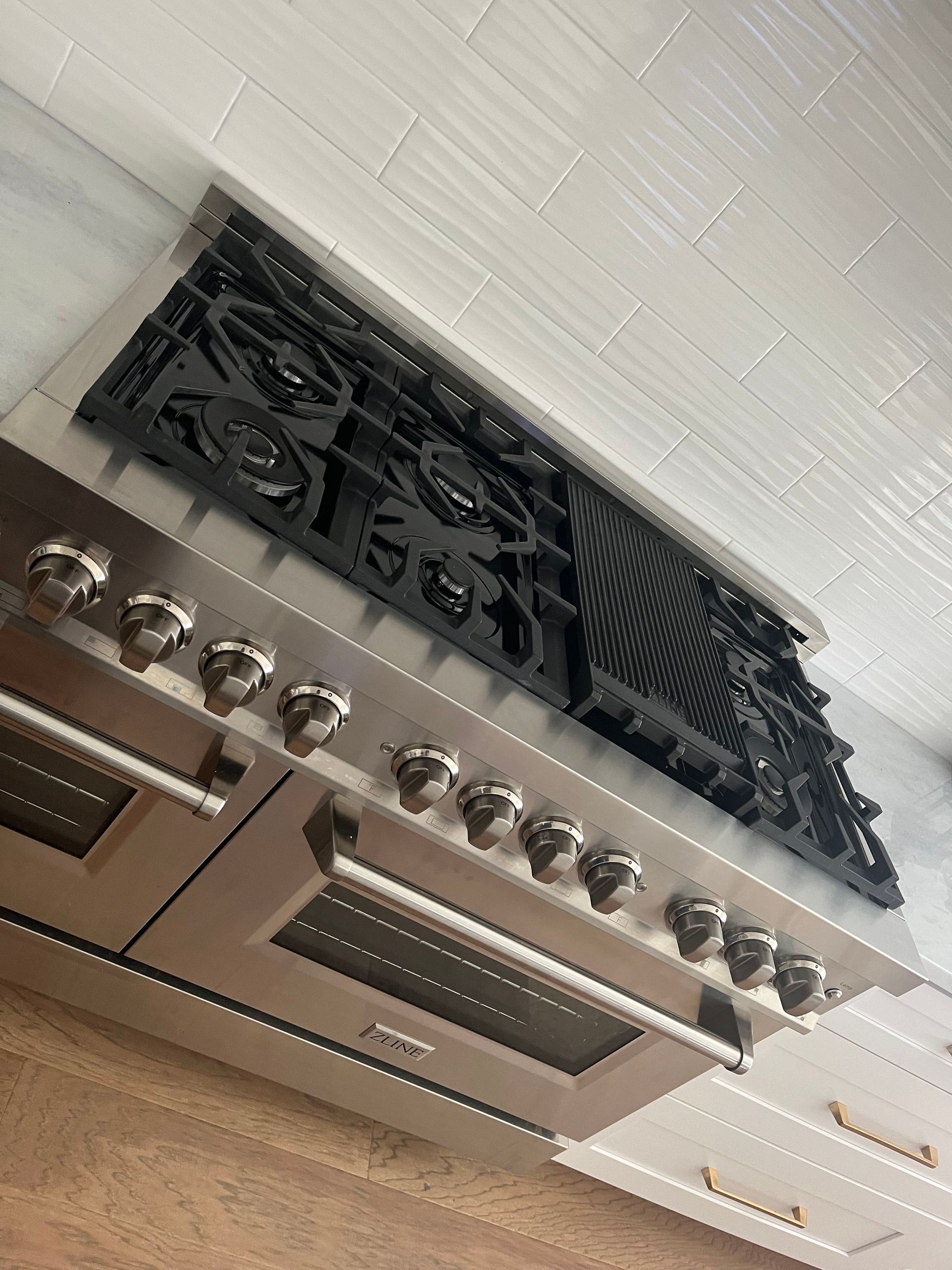 A high-end, stainless steel professional dual-oven range with a black gas cooktop and griddle in a bright kitchen.