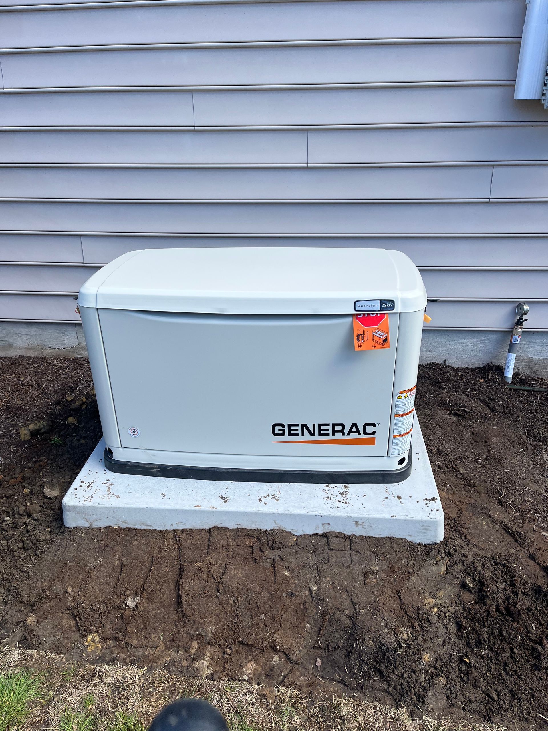 A light gray Generac standby generator sits on a concrete pad against the side of a house with light gray siding.