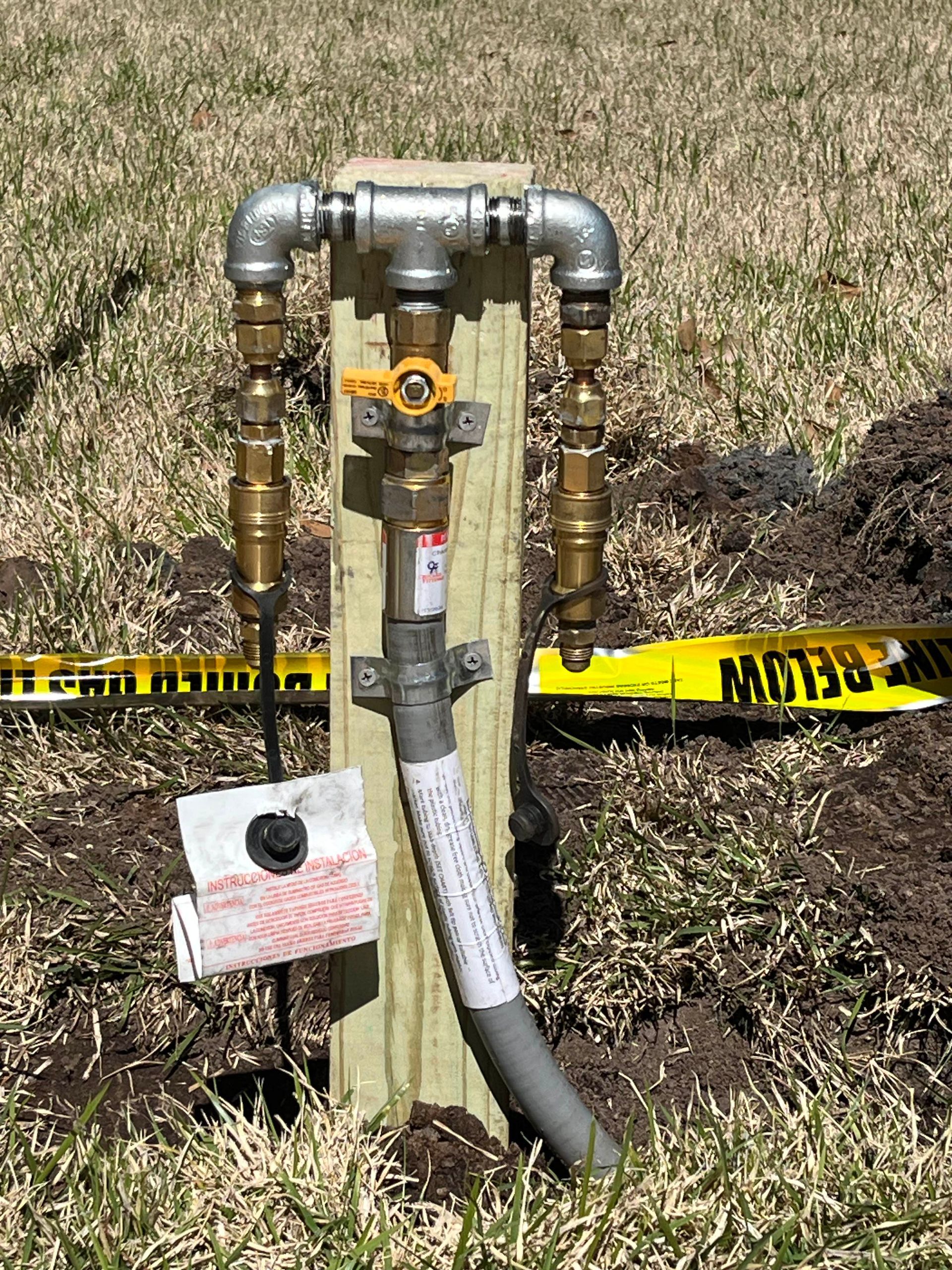 An outdoor natural gas riser with a shut-off valve mounted to a wooden post, surrounded by yellow hazard tape.