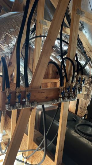 A plumbing manifold with several black hoses attached to a wood frame in an attic or crawl space.
