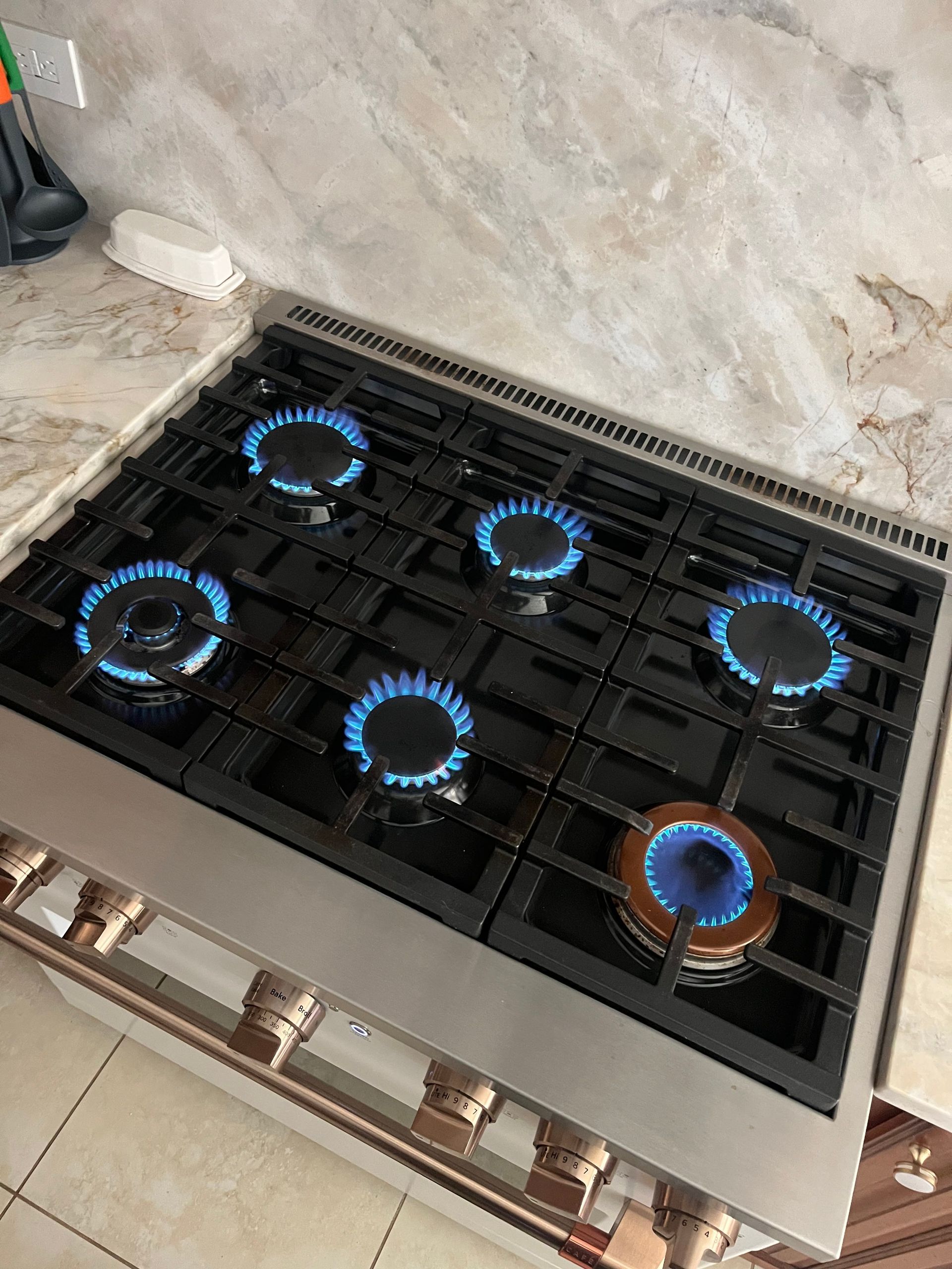 A stainless steel gas cooktop with five burners lit with blue flames, set into a light-colored countertop.