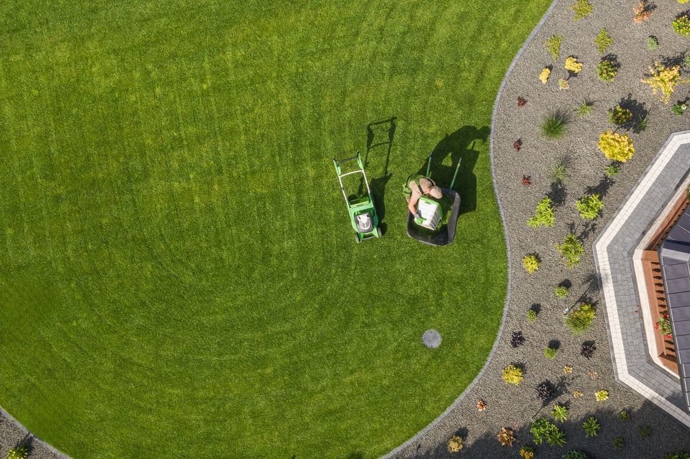 Aerial view of a person mowing a large, curved lawn with a push mower and a riding mower.