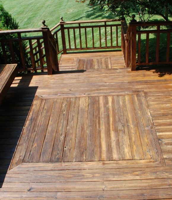 Wooden deck with a large, square access panel and railings, leading to a green lawn.