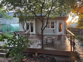 Backyard deck with modern metal railing, small house, and mature tree.