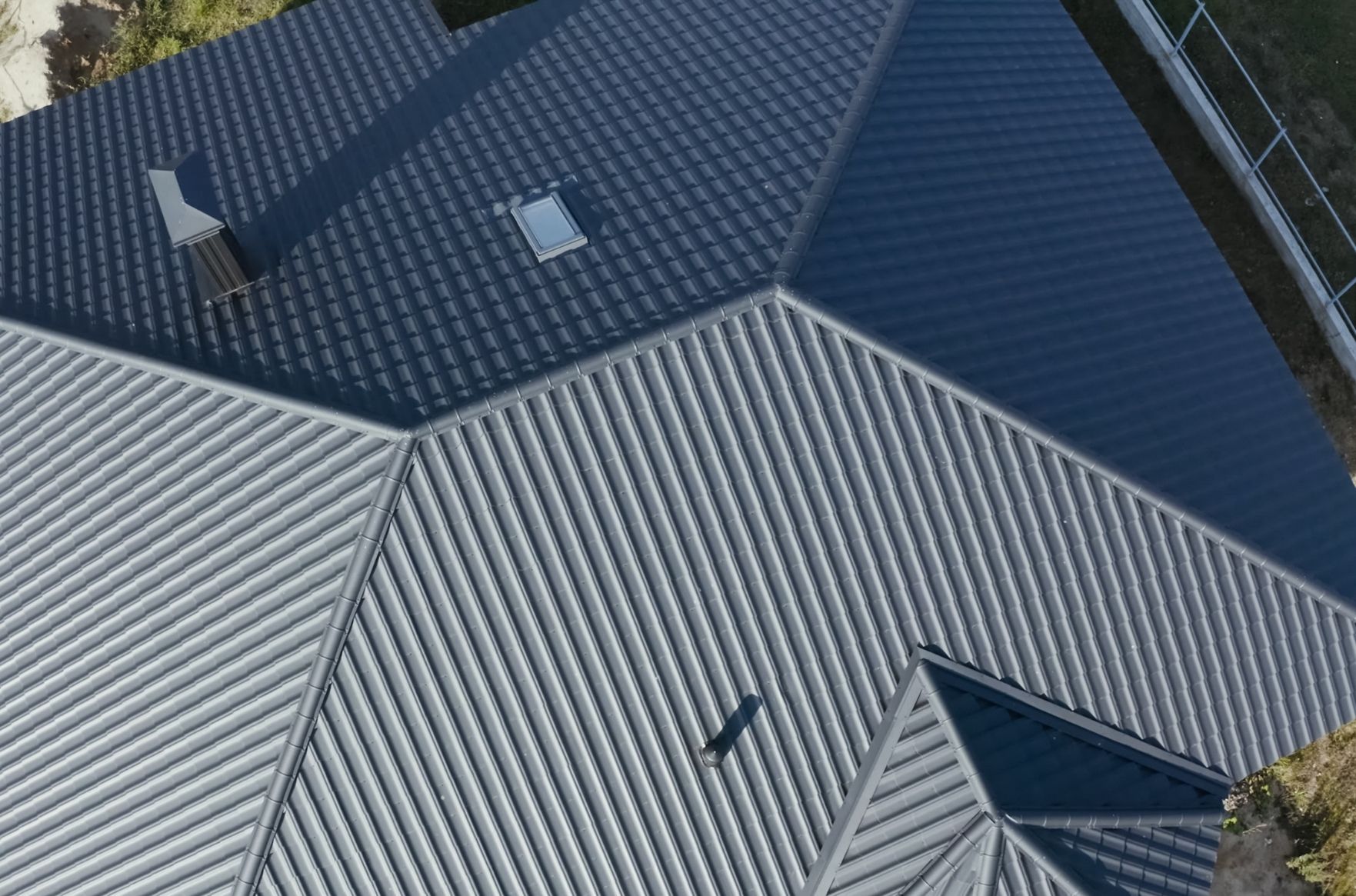 A high-angle aerial view of a residential metal roof with contrasting grey and dark blue paneled sections.