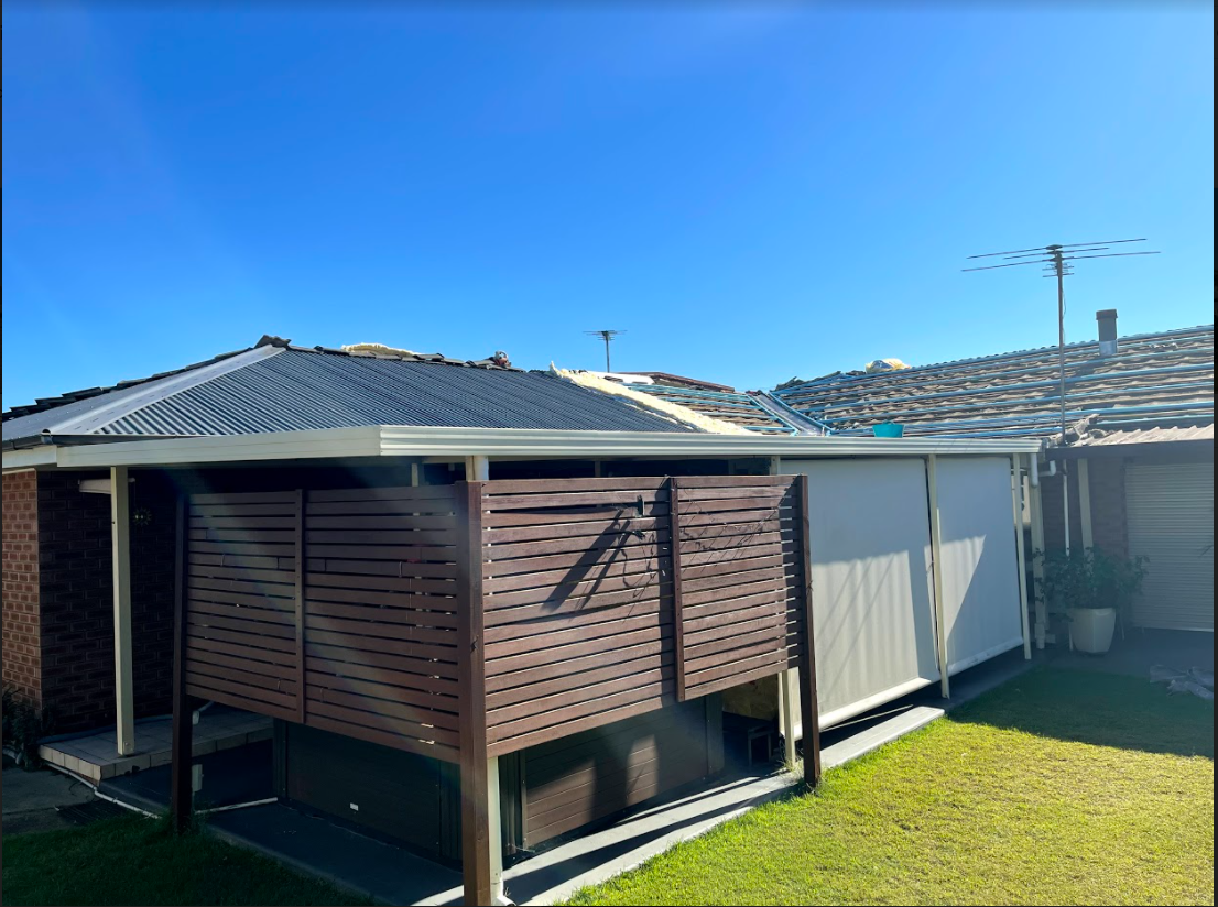 A patio area under a dark roof featuring a wooden privacy screen, light-colored privacy curtains, and a grass lawn.