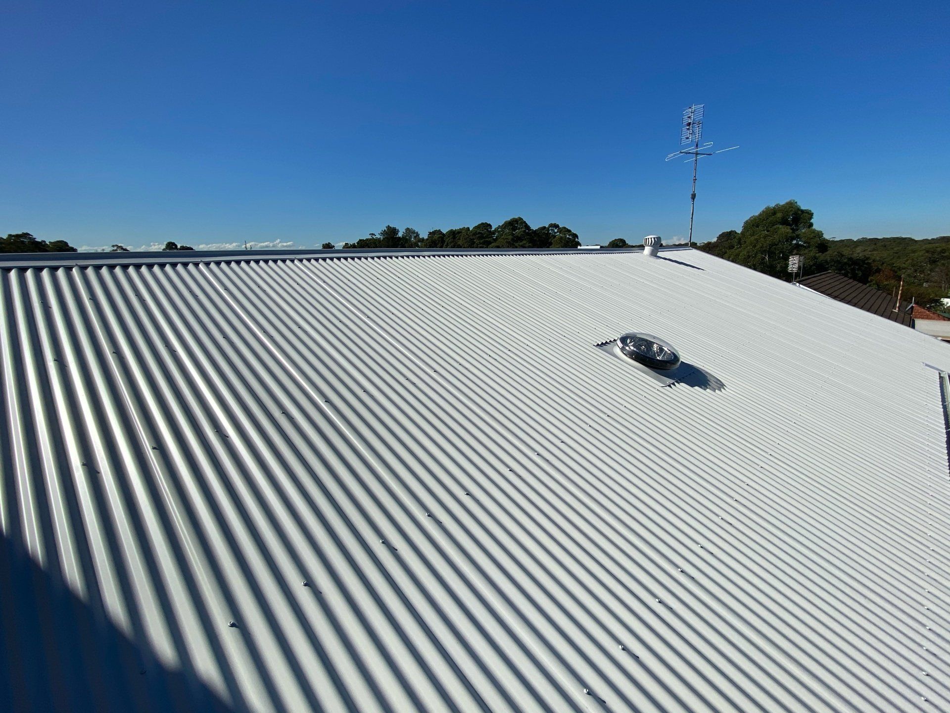 A white, corrugated metal roof under a bright blue sky, with a roof vent and a TV antenna visible.