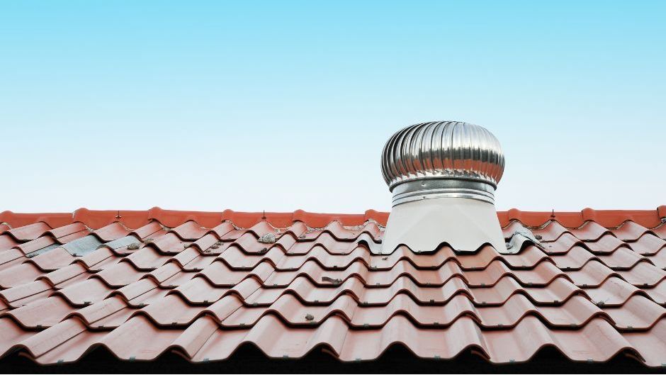 A metallic roof ventilator installed on a red corrugated roof against a clear blue sky.
