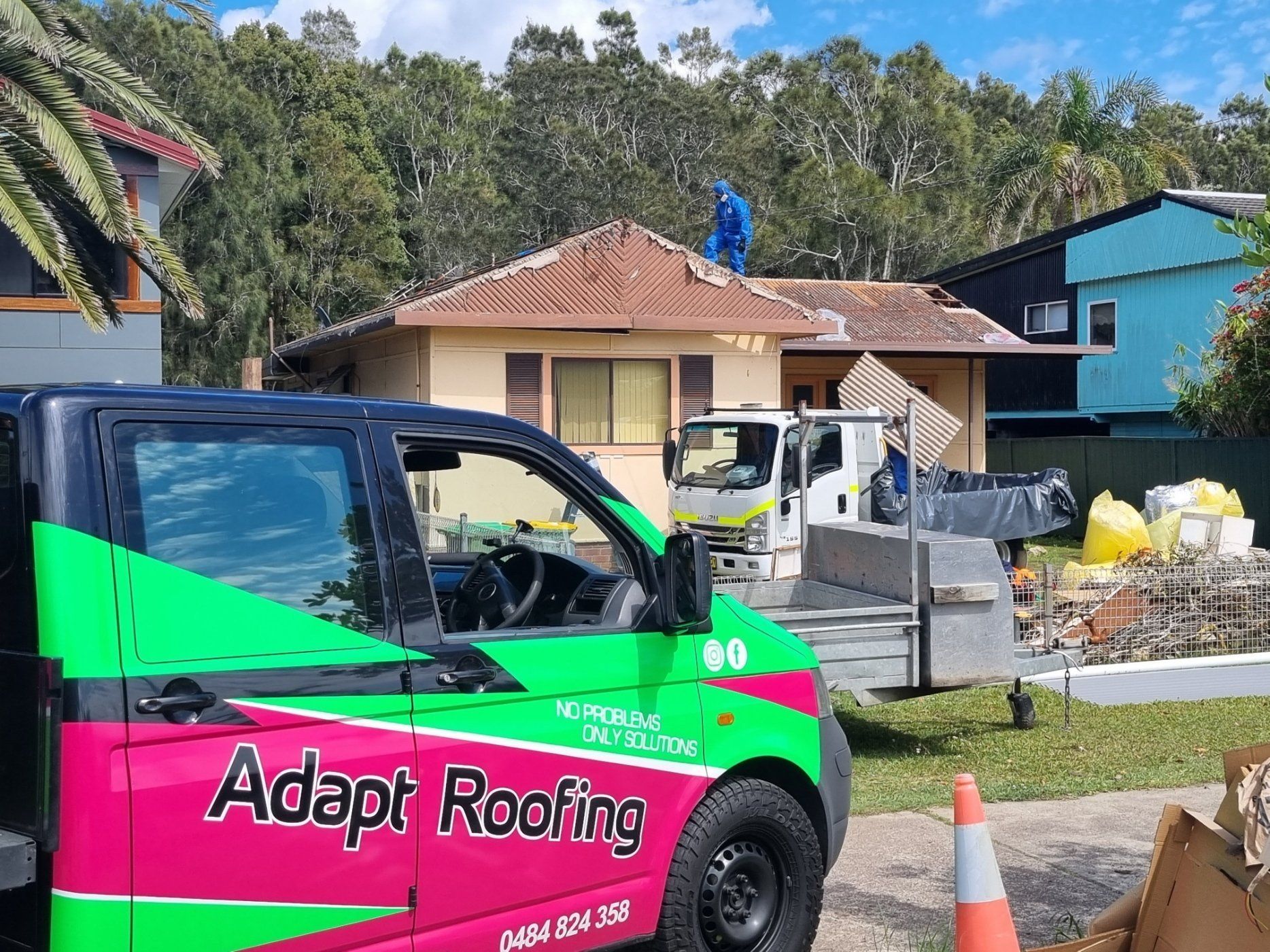 A bright pink and green Adapt Roofing utility truck parked in front of a house where a worker is on the roof.