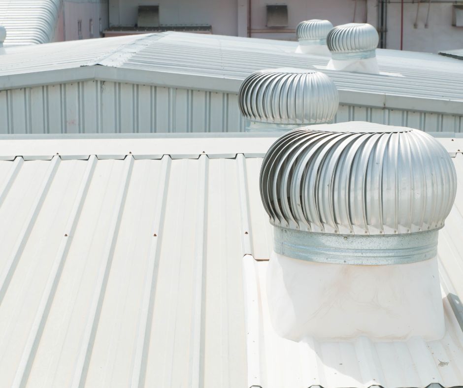 Silver industrial roof turbine ventilators mounted on a metal-paneled rooftop.