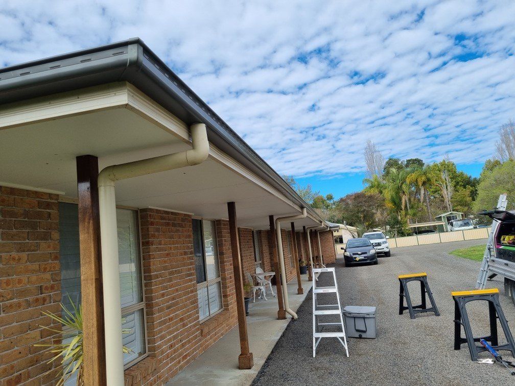 A brick building with an overhanging roof and a row of support posts, with a ladder and construction equipment nearby.