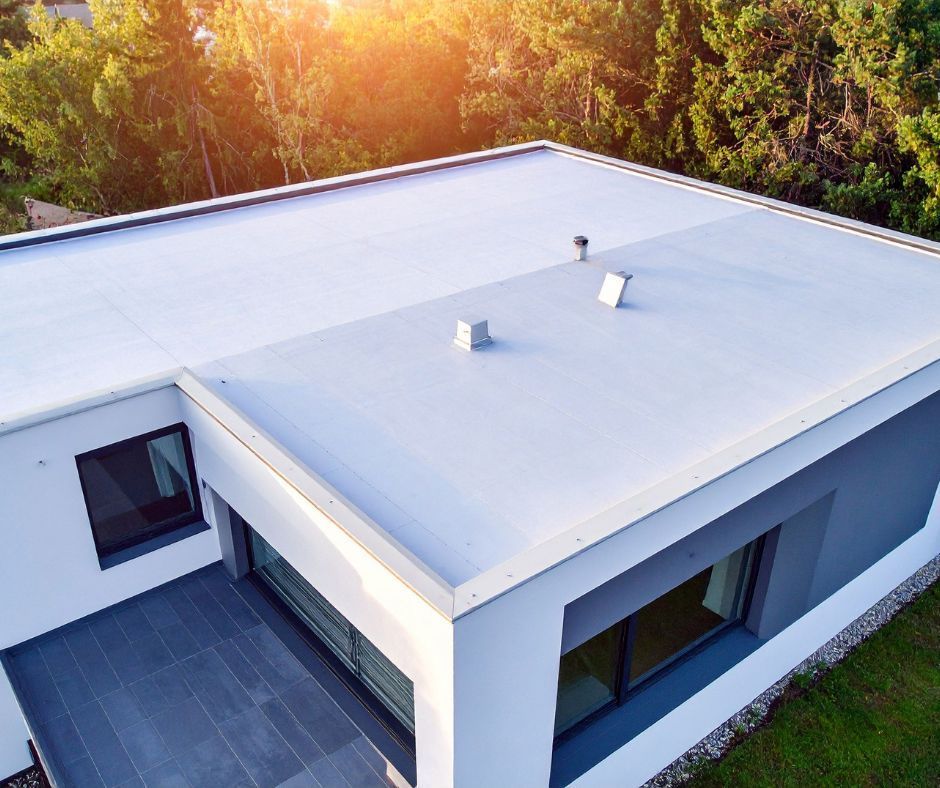 Modern white flat-roof house viewed from above, surrounded by trees.