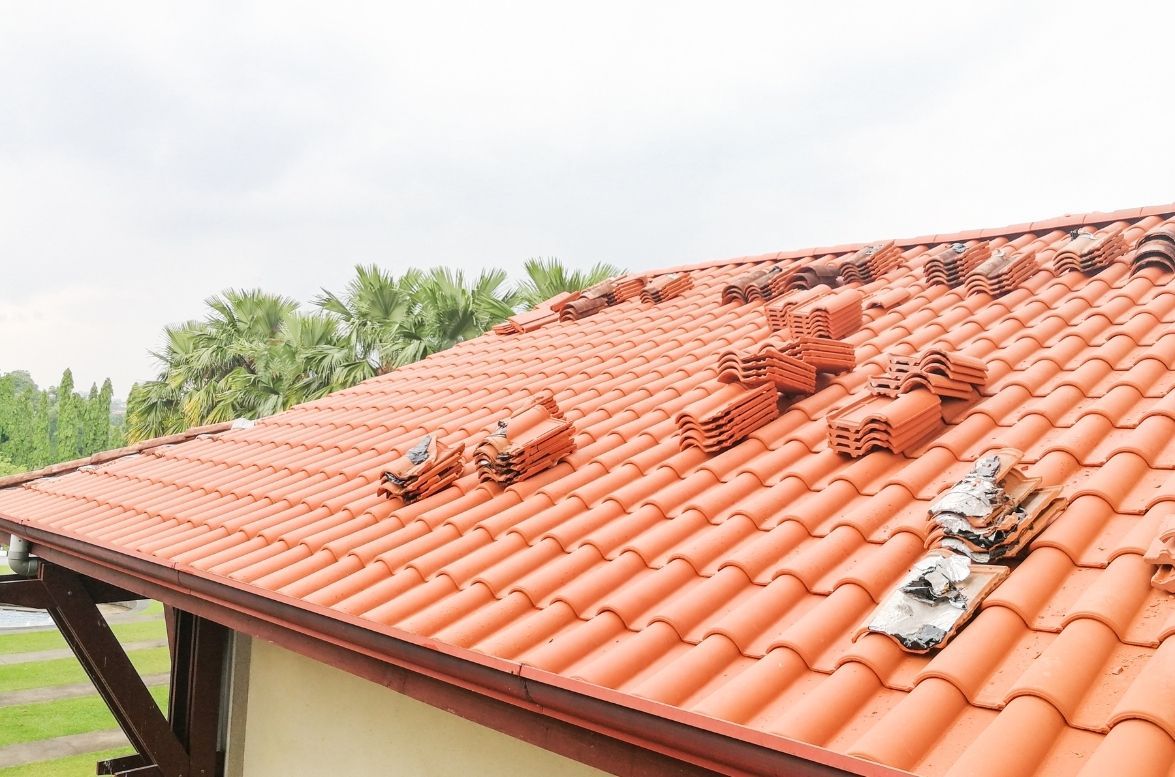 A sloped roof covered in red ceramic tiles, with scattered piles of spare tiles resting on the surface.