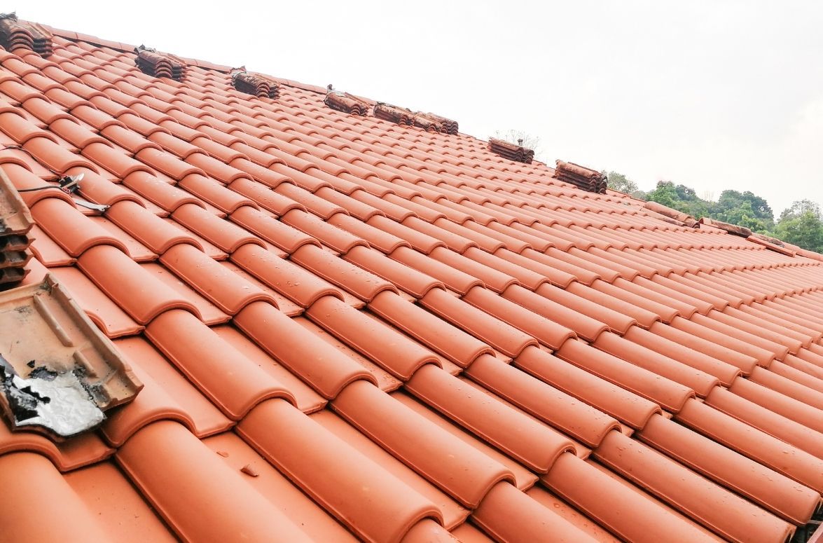 A close-up view of an orange terracotta tiled roof with some damaged or missing tiles near the eaves.