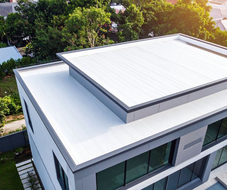 Modern white flat-roof house with rooftop, surrounded by trees.