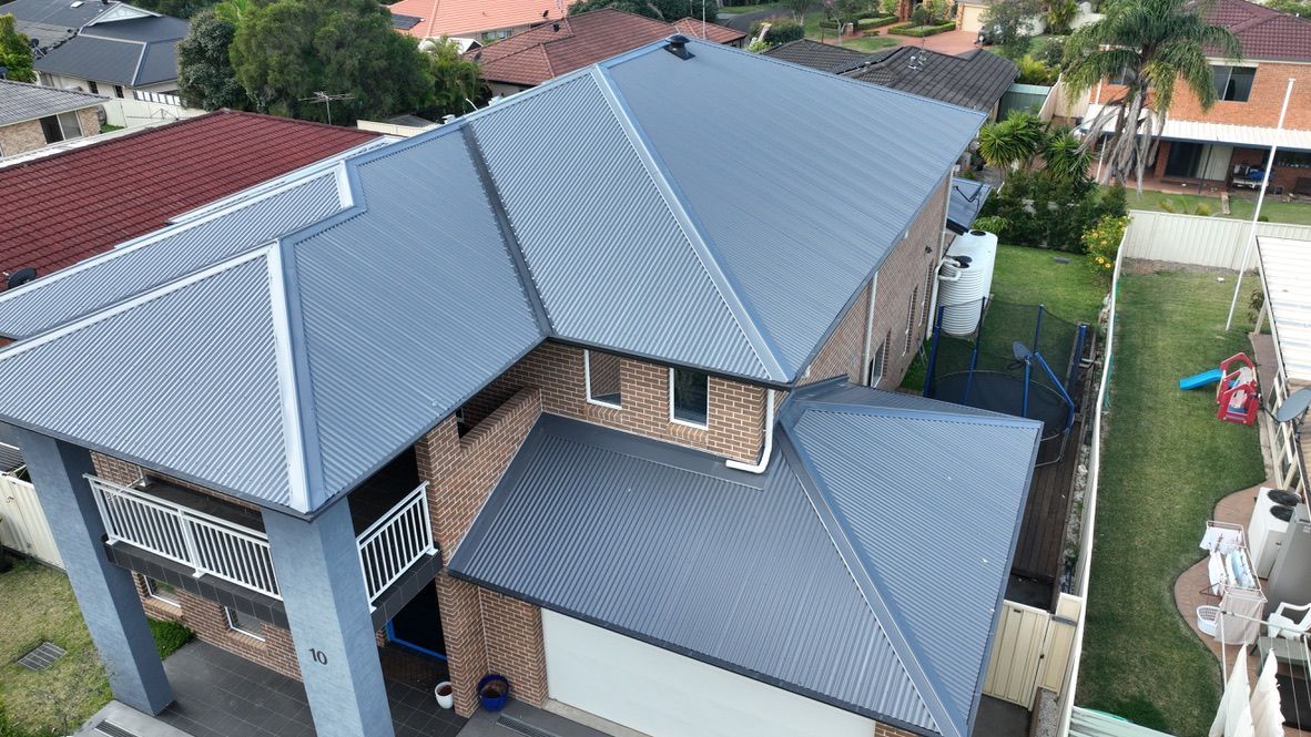 An aerial view of a two-story residential house with a gray corrugated metal roof and a brick exterior.