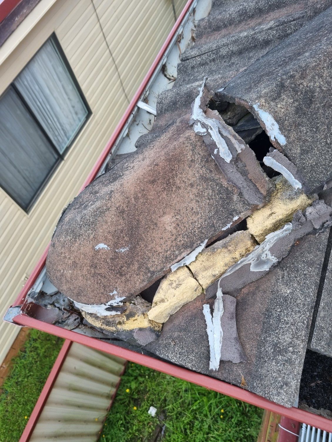 A damaged concrete roof tile section showing visible mortar repairs and a gap, located near a home gutter and window.