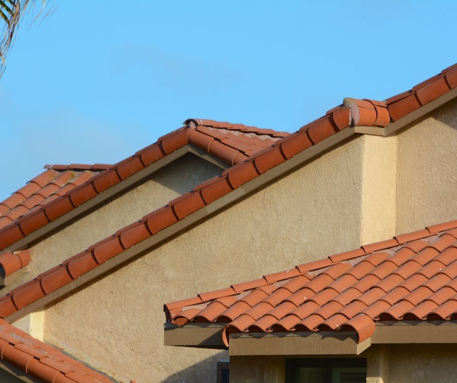 A section of a stucco house exterior featuring a multi-tiered roof with terracotta clay tiles under a clear blue sky.