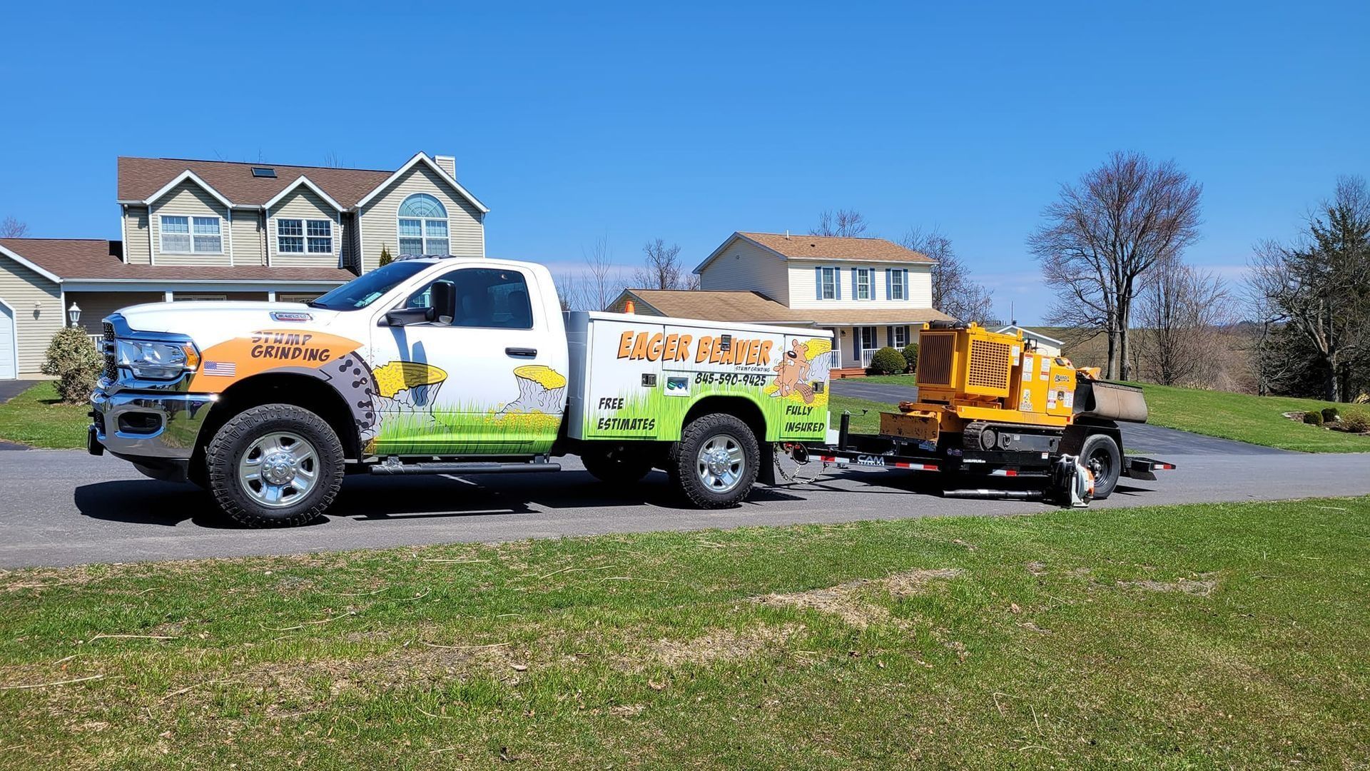 White work truck hauling a yellow trailer-mounted machine on a suburban street, with houses and lawn in the background