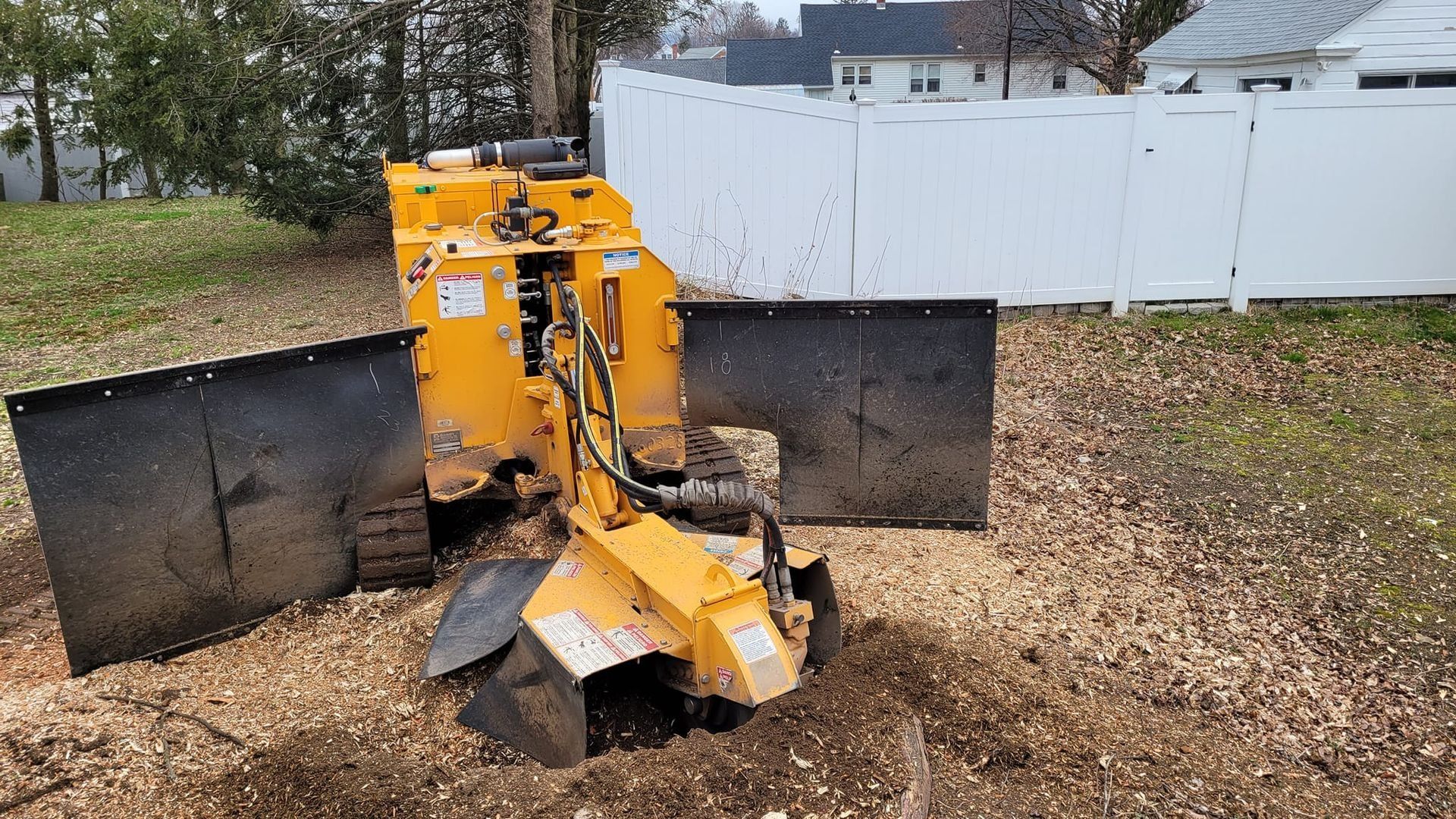 Yellow snowplow blade attachment on a gravel driveway beside a white fence in a backyard