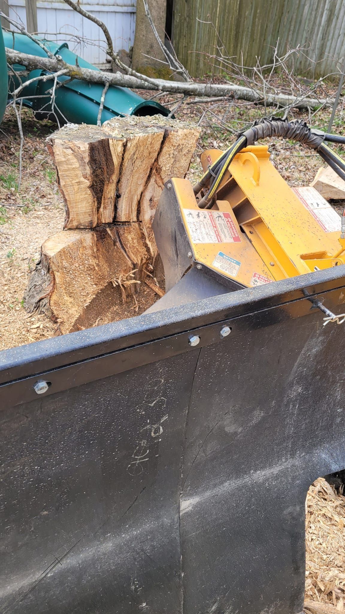 Yellow chainsaw resting on a black trailer beside stacked cut logs outdoors