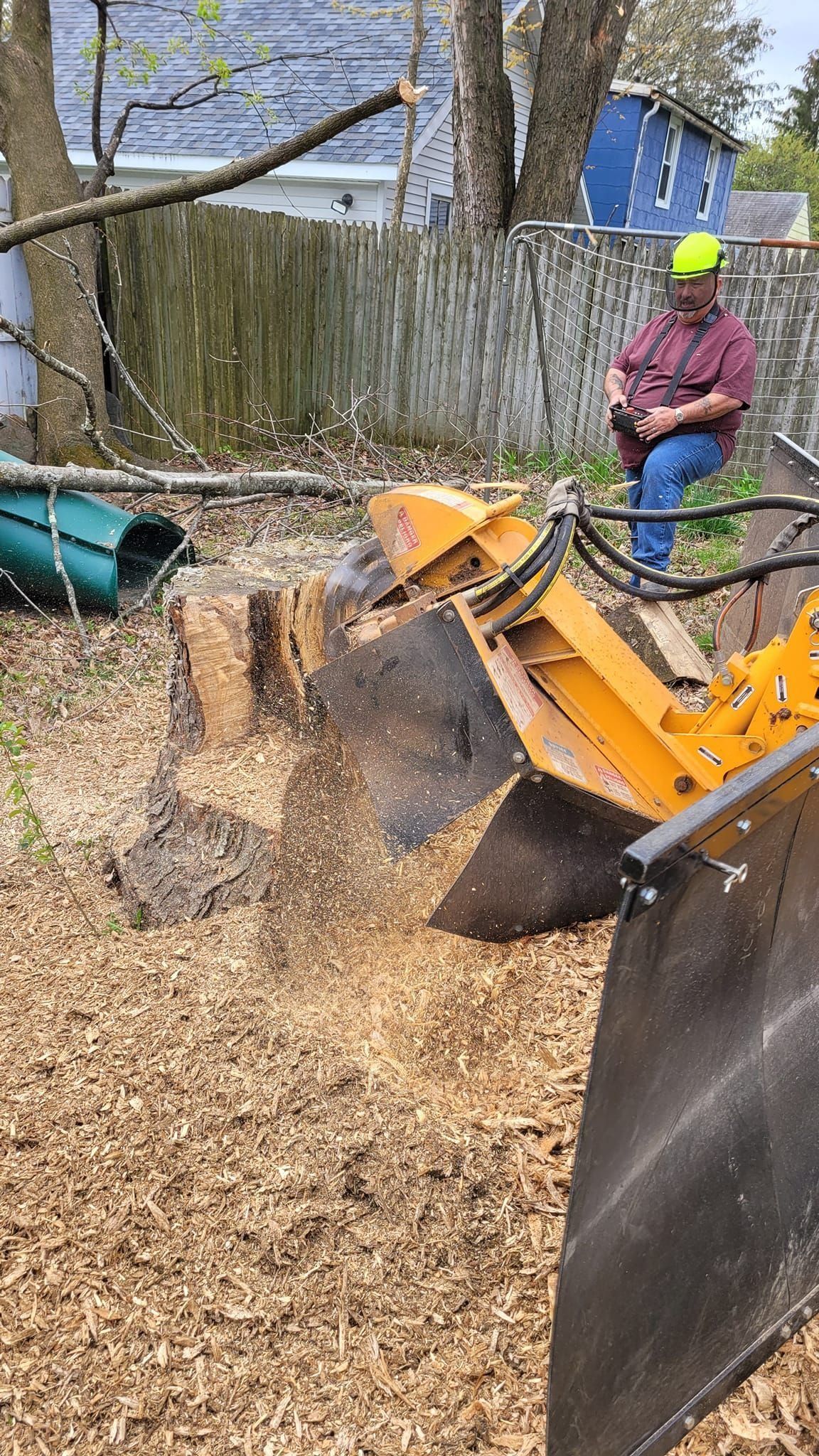 Worker in neon helmet using an orange wood chipper to clear a yard full of mulch debris
