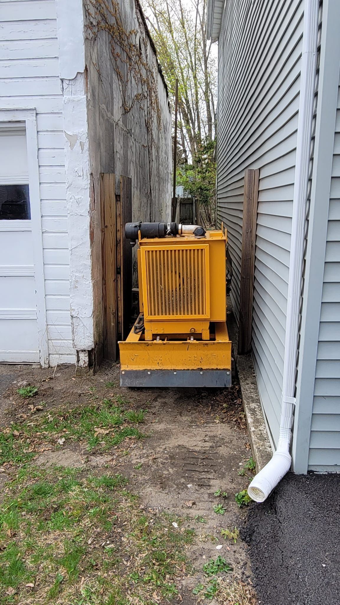 Yellow generator beside a white house in a narrow side yard between two buildings