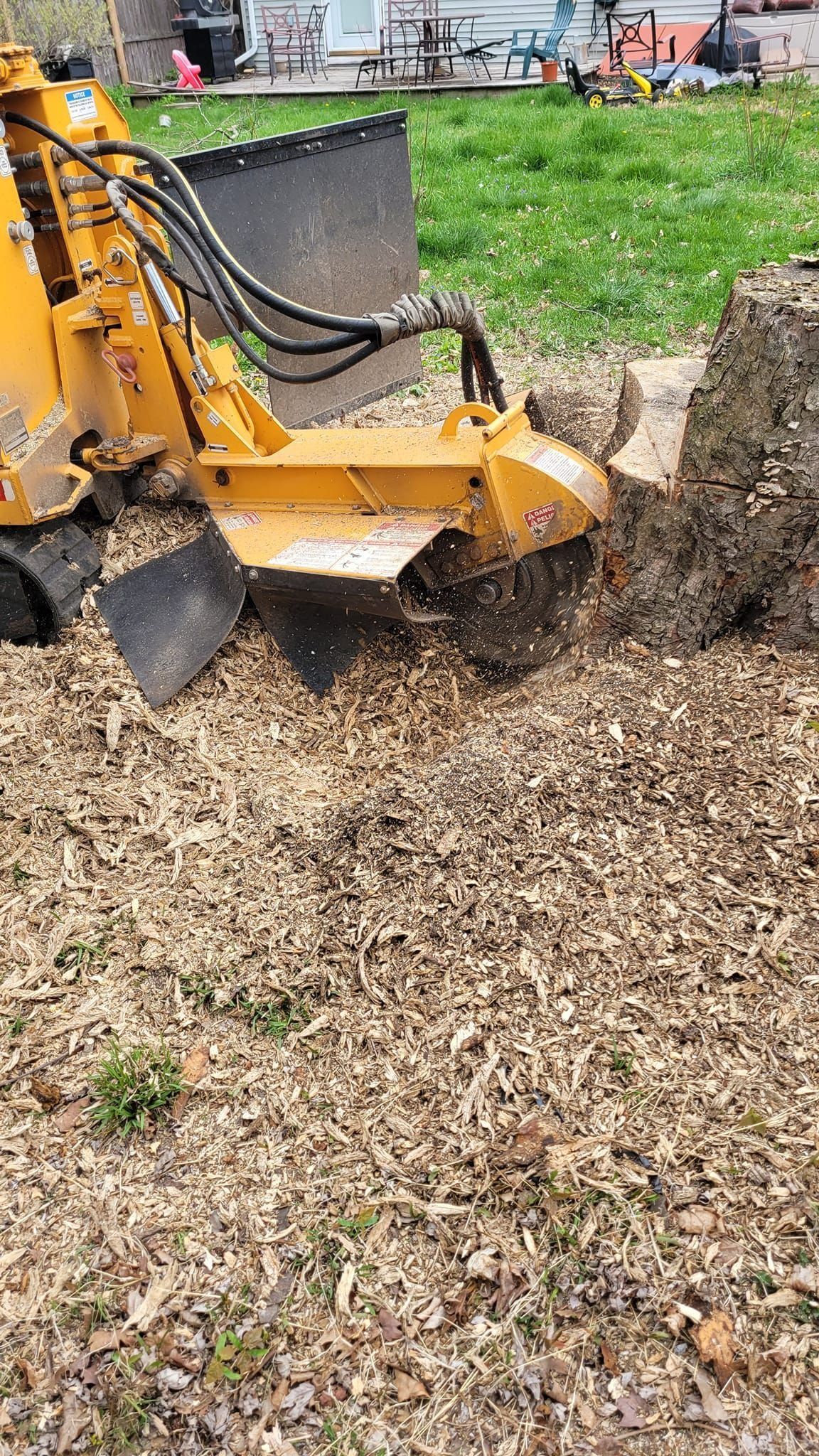 Yellow excavator bucket digging into soil and wood chips beside a grassy area