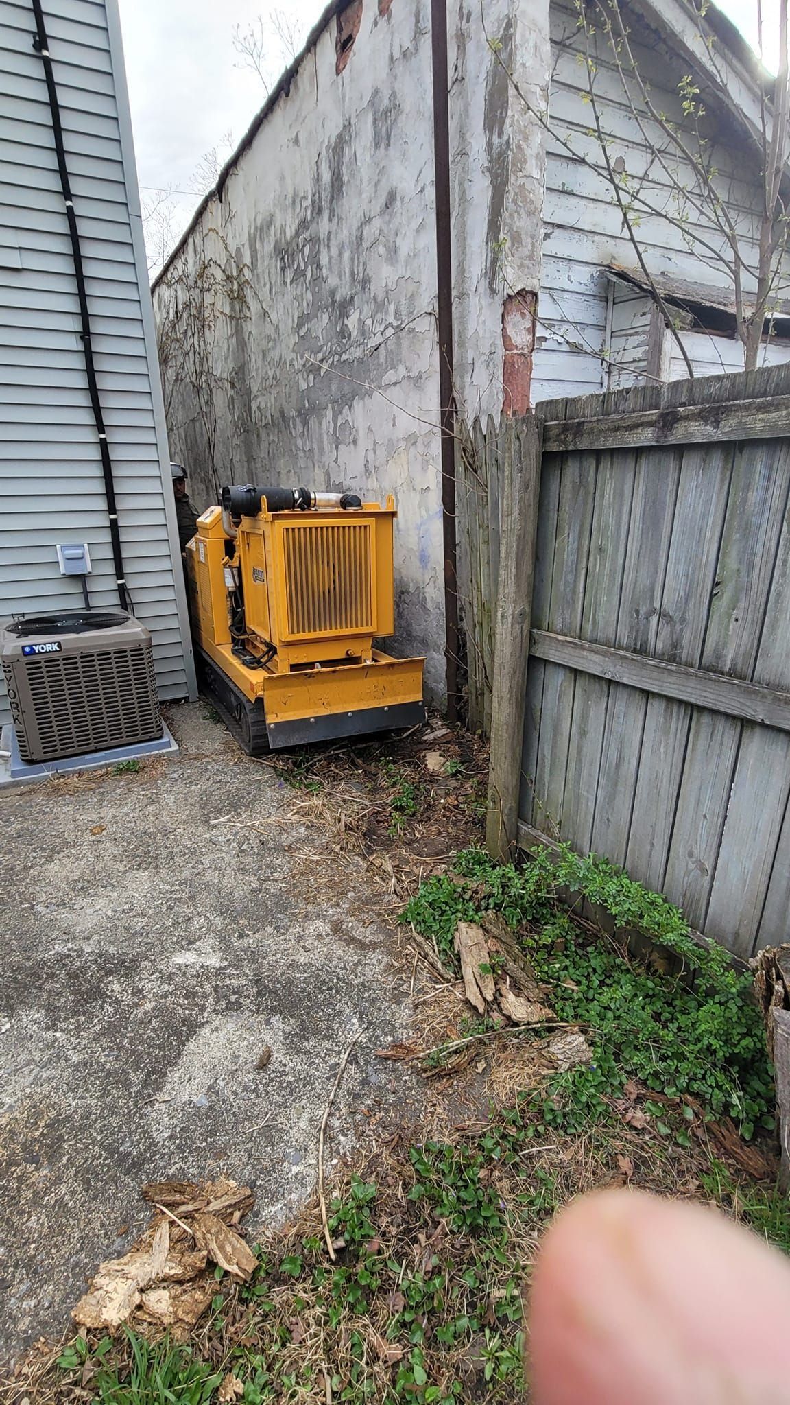 Yellow mini excavator parked in a narrow gravel alley beside weathered concrete walls.